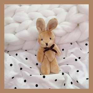 Close-up of soft plush rabbit keychain with brown bow on white knitted background