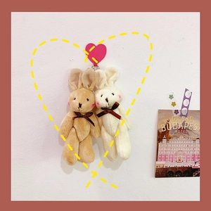 Close-up of cute plush bunny keychains in white and brown with silk bows and metal hooks