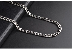 Close-up of polished silver stainless steel Cuban link chain on a dark textured surface