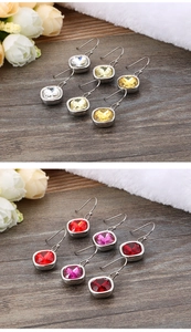 Close-up of square zircon earrings in multiple colors on a dark wooden surface