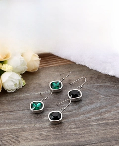 Detail of square-cut green and black zircon drop earrings on a rustic wooden background