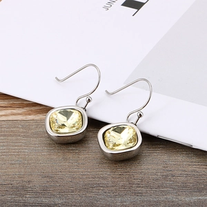 Square yellow zircon drop earrings with silver metal hooks on a magazine background
