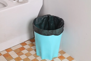 Blue wave-edge trash bin with thickened black liner shown in a bathroom corner setting