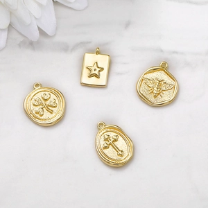 Golden metal clover, star, bee, and cross pendants on marble surface with white flowers