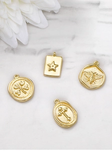 Detail of vintage gold metal charms with star, bee, clover and cross relief patterns