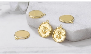 Close-up of golden bee relief and oval metal charms on white marble background
