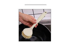 Close-up of beige long handle cleaning brush with stiff bristles used on a black cooking pot