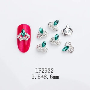 Detail view of emerald crown nail charms on red manicured nail and loose silver pieces