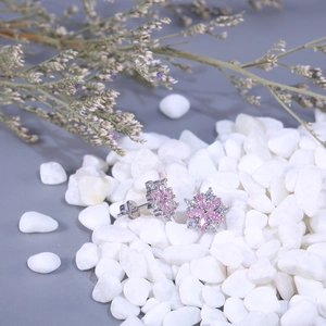Close-up of pink zircon flower earrings with silver metal petals on white pebbles