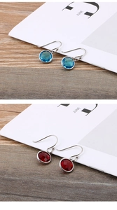 Close-up of titanium steel earrings with round cut blue and red gemstones on wood