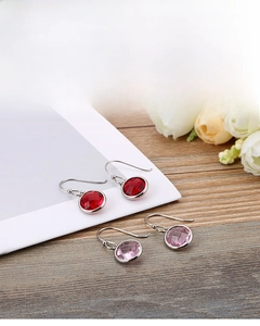 Detail shot of elegant red and pink round cut gemstone earrings on wood and floral background