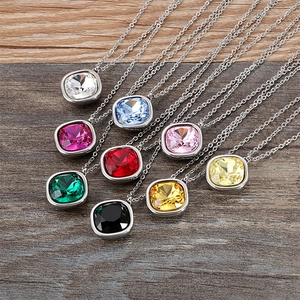 Elegant silver chain necklaces with various colorful square gemstone pendants on wood