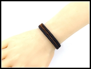 Detail view of a handwoven dark brown leather bracelet on a wrist with adjustable design