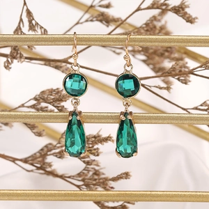 Long geometric gold earrings with emerald green teardrop crystals on a metallic stand
