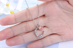 Detail of silver moon crescent pendant with pink crystal bead held by hand