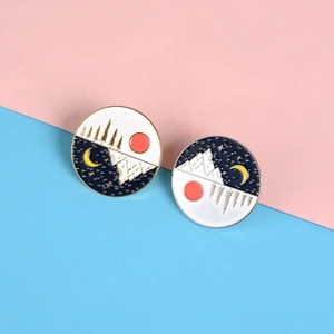 Detail of round enamel pins showing day and night landscapes with mountains and sun