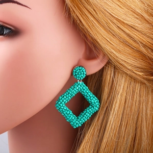 Handmade turquoise geometric rhombus beaded drop earrings worn on a model