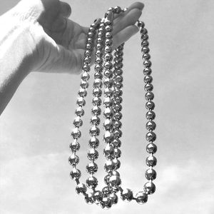 Artistic monochrome view of a polished stainless steel bead chain necklace held by hand