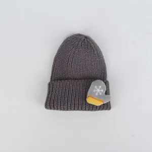 Dettaglio del cappello in maglia grigio scuro con toppa a guanto e fiocco di neve