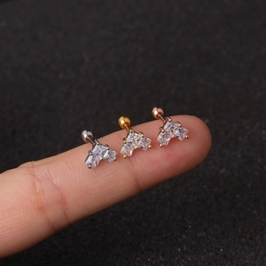 Detailed close-up of mini flower cartilage studs in silver, gold, and rose gold on a finger