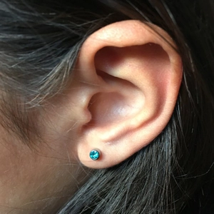 On-ear view of a 316L stainless steel stud earring with a round sky blue gemstone