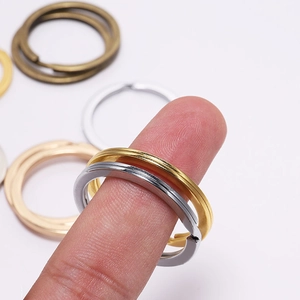 Polished metal key rings in various sizes and colors displayed on a finger for scale