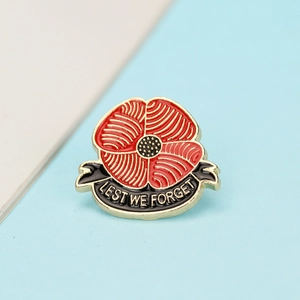 Detail of red enamel poppy brooch with gold trim and Lest We Forget ribbon text