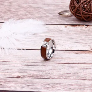 Modern stainless steel ring with walnut wood inlay and circular accent on wooden background