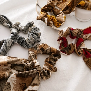 Close-up of four snake print hair scrunchies in brown and grey tones on white silk