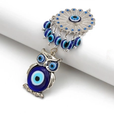 Detail of silver owl charm and evil eye beads set on a white cylindrical display base