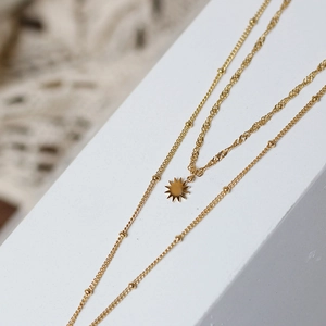 Macro shot of double-layered gold necklace with sun pendant on white geometric blocks
