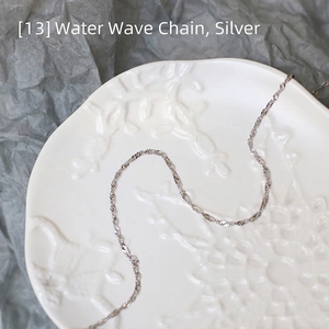 Macro shot of silver water wave chain necklace in a decorative white porcelain dish