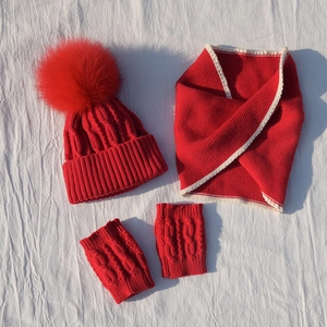 Detail of red cable-knit children's winter set including pom-pom hat, scarf, and mittens