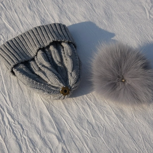 Close-up of gray cable-knit winter hat with detachable pom-pom and metal snap fastener