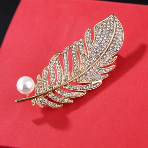 Detailed close-up of golden feather brooch with white crystals and a round pearl