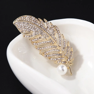 Elegant gold feather brooch with shimmering rhinestones and a white pearl on black background