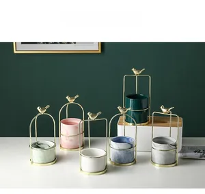Detail of Nordic ceramic planters with bird-shaped gold metal stands and marble finish