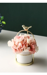 Detail of pink hydrangea in white ceramic vase with golden metal bird handle stand