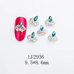 Detailed macro of silver crown nail art studs with green rhinestones on red nails