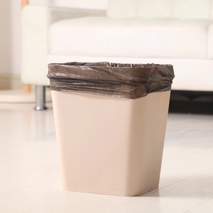 Thickened beige waste bin with black liner bag on light floor against a white sofa