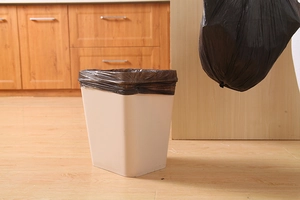Close-up of thick black drawstring trash bags in a beige bin against wooden kitchen floor