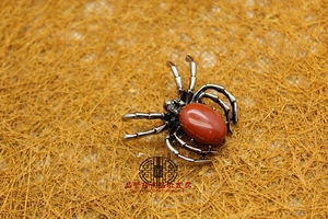 Macro detail of silver spider brooch featuring a large red oval gemstone on a textured background