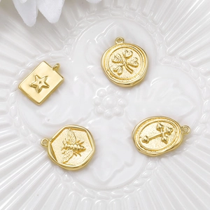 Set of four gold metal charms with star clover bee and cross patterns on white ceramic