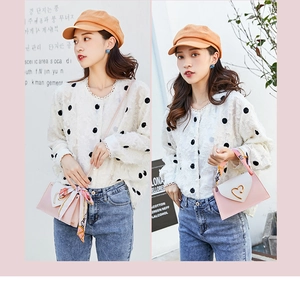 Detail of pink and white handbag featuring a heart-shaped metal clasp and silk scarf handle