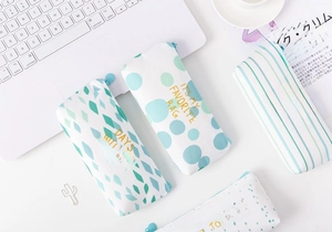 Detailed flat lay of four canvas pencil cases with gold prints on a white office desk