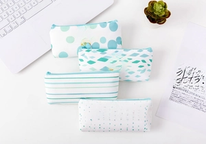 Detail of four canvas stationery bags with gold foil text and mint green patterns on a desk