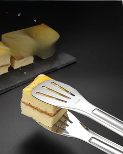 Nahaufnahme der SUS 304 Edelstahl-Küchenzange, die ein Stück Kuchen auf Schiefer greift
