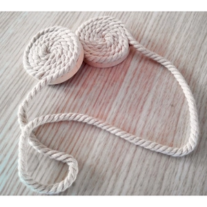 Detail view of cream-white hand-woven cotton curtain tiebacks on a wooden surface