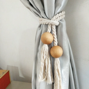 Detail of handwoven cotton curtain tieback with wooden beads and tassels on fabric