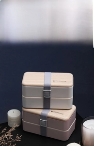 Close-up of double-layer lunch box with wood-style lid and elastic strap detail